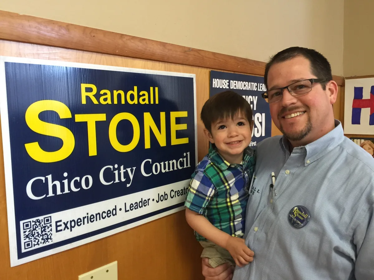 Randall Stone holding his young son beside a Randall Stone for Chico City Council campaign sign